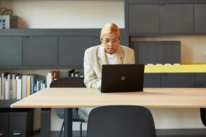 Retail store manager working on a laptop in an office space. Keywords: One person; mobile device; on the go; woman; female manager; furniture; HR; operations; security; Dynamics 365; decision maker