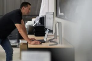 Security practitioner looking at desktop screens and working to investigate threats. Keywords: Security; operations; man; standing; laptop; threat hunting