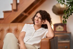 A portrait of a woman sitting on a couch, leaning on the arm rest.