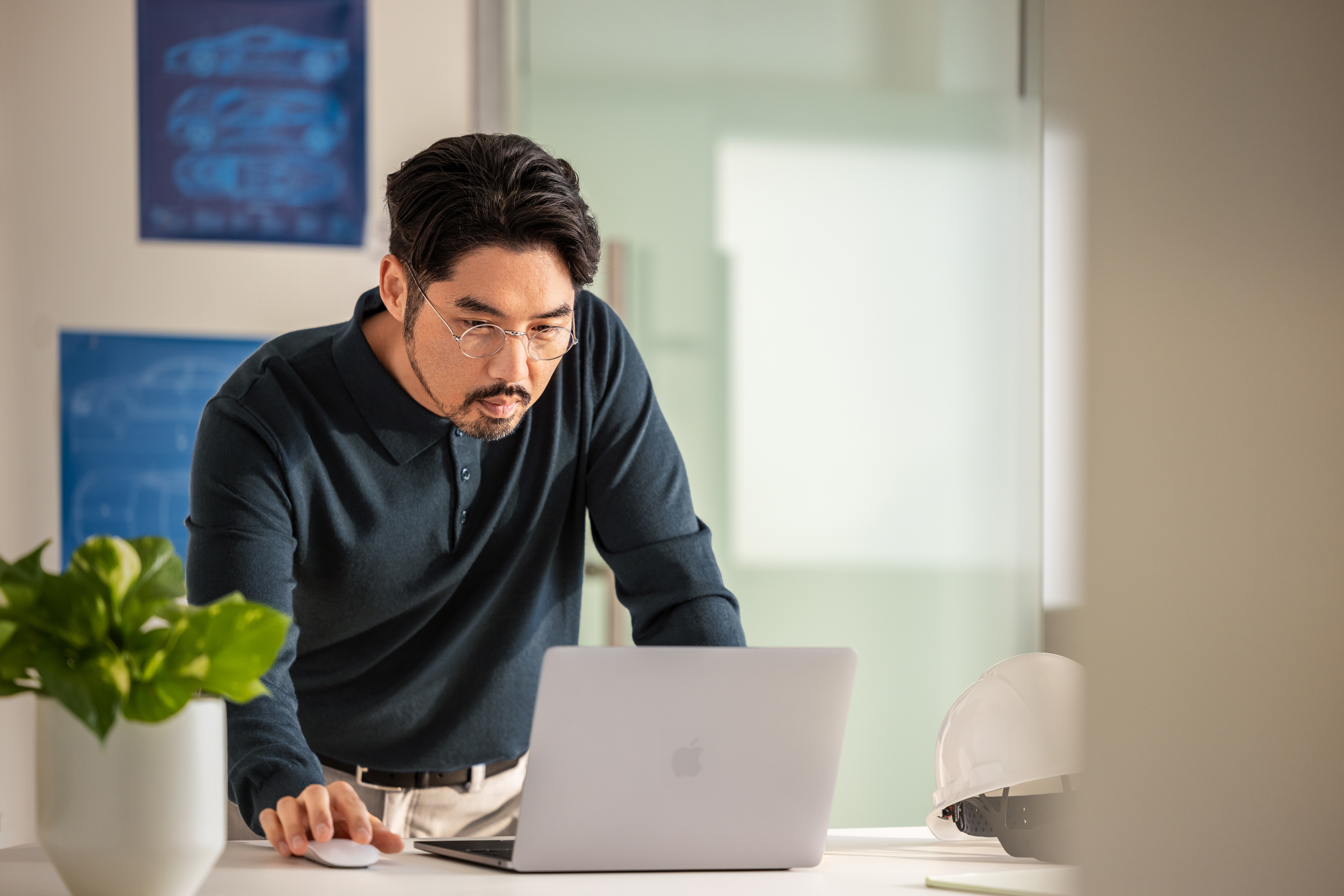 A man in a blue shirt and glasses looking at a laptop