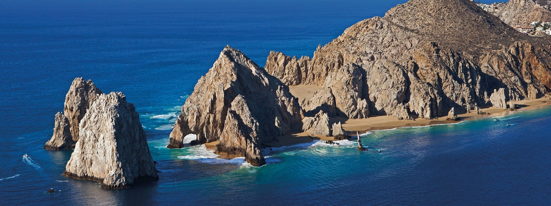 a rocky island in the middle of a body of water with Arch of Cabo San Lucas in the background