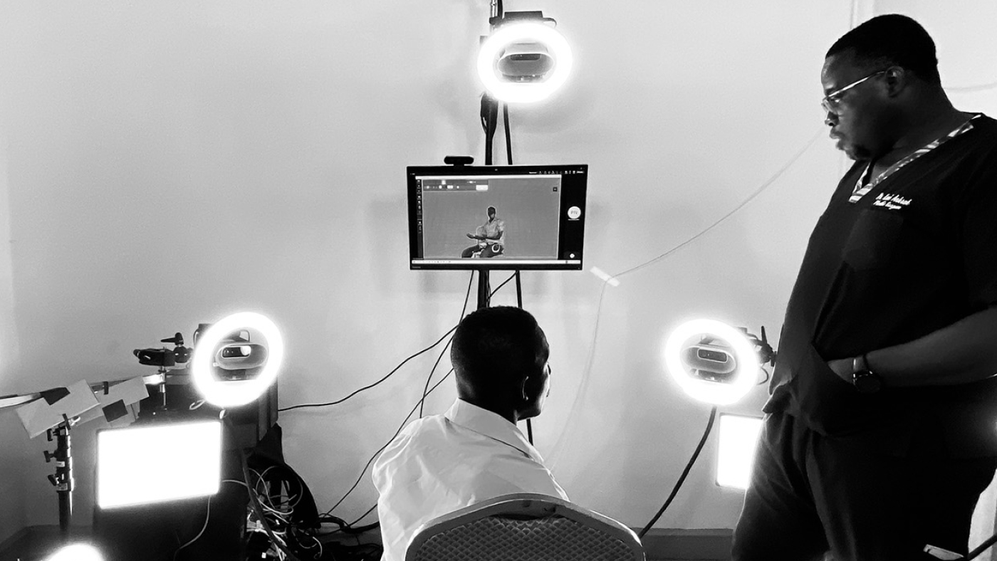 A picture captured at the Telemedicine rig in Accra depicting a male black patient seated inside the rig, with multiple Azure Kinect cameras positioned around him. He is engaged in a conversation with a doctor standing beside him.