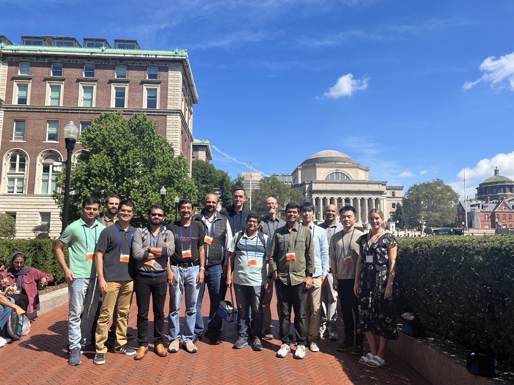 a group of researchers attending SIGCOMM 2023. They are standing in front of multiple buildings.