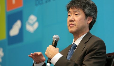 Peter Lee wearing a suit and tie holding his hand up