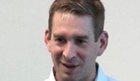 a man wearing a suit and tie smiling at the camera