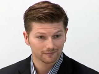 a man wearing a suit and tie smiling at the camera