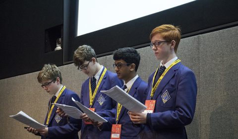 a man wearing a suit and tie talking into a microphone