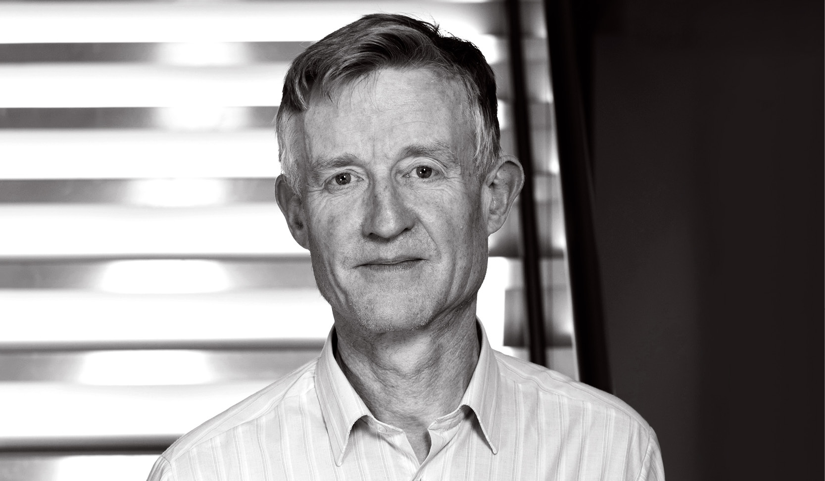 Simon Peyton Jones wearing a suit and tie smiling and looking at the camera