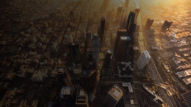 Downtown Los Angeles during a hazy sunset from a helicopter. The light rays shine gold from in between the building of DTLA.