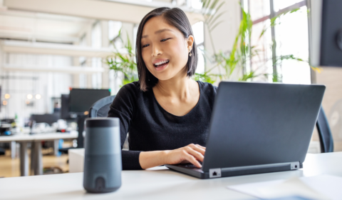 a woman sitting at a table with a laptop and smiling at the camera
