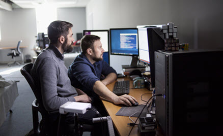 Image of two workers collaborating on a desktop PC.