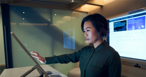 An image of a woman wearing a dark shirt in a dim office scrolling or working on a Microsoft Surface Studio.
