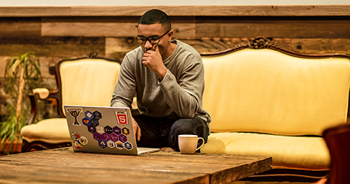 An image of a man sitting on a couch working remotely with his laptop.