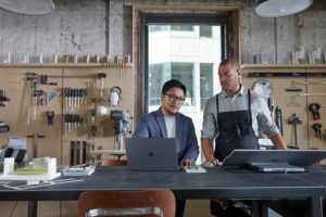 Two adult male collaborating in architecture modeling studio looking together on a platinum Microsoft Surface Laptop 3 and a platinum Microsoft Surface Studio 2.