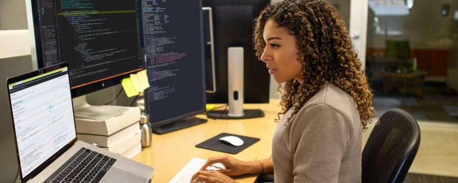 Black female developer working at enterprise office workspace. Focused work. She has customized her workspace with a multi-monitor set up.