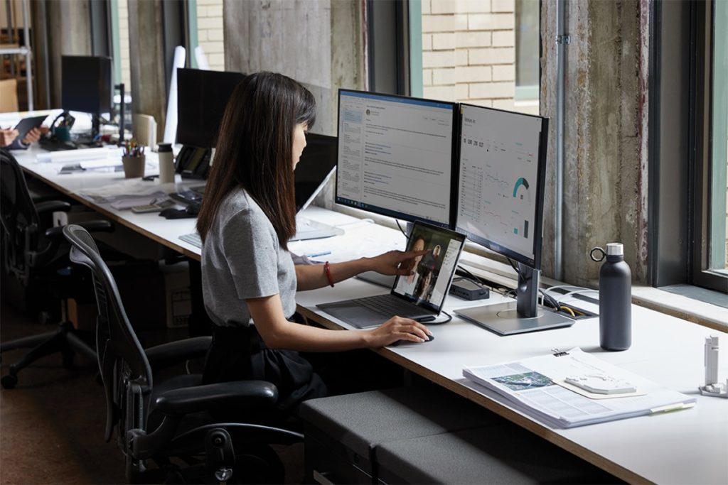 Adult female sitting at a desk in an office environment with a Microsoft Surface Laptop 3 using touchscreen to scroll.