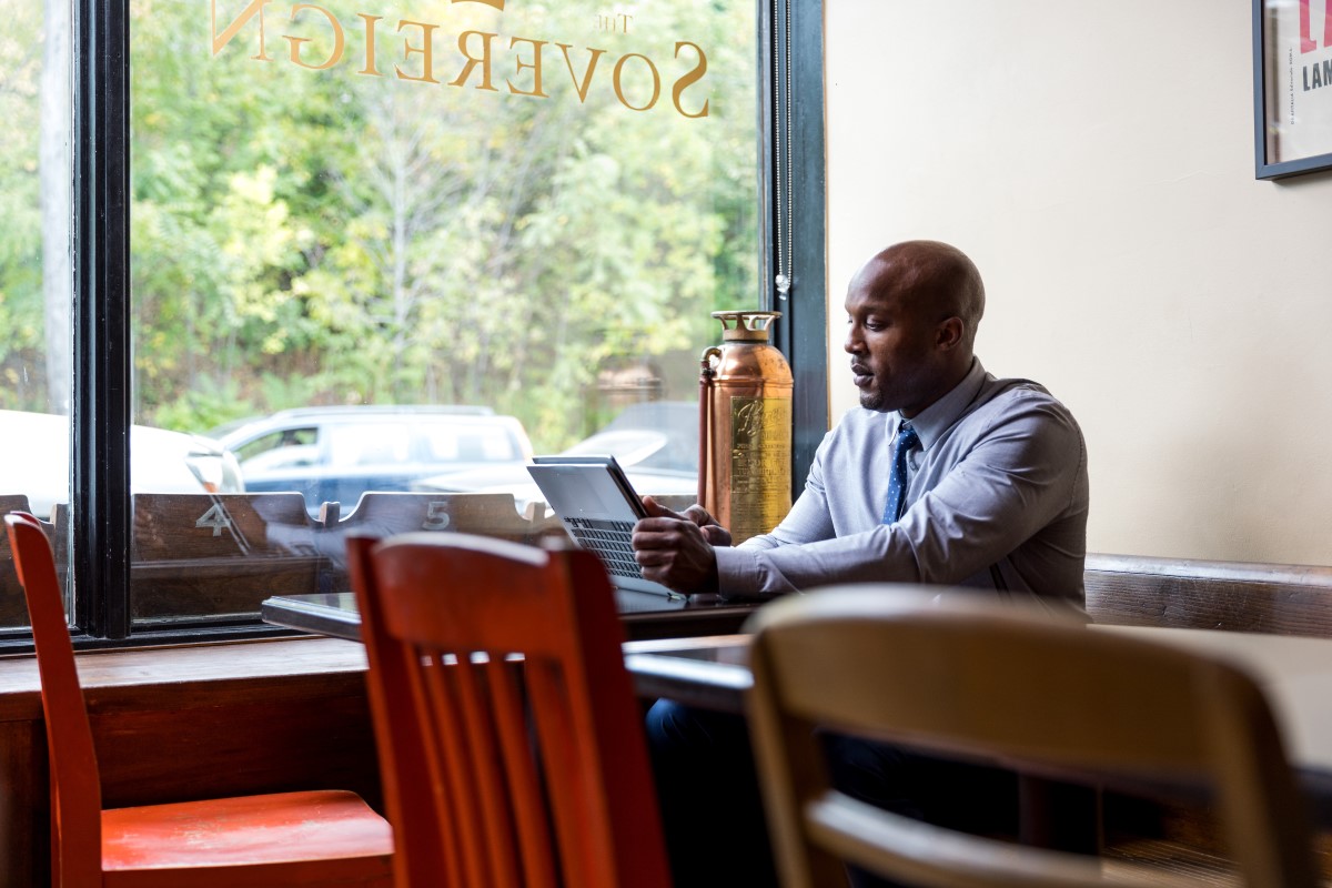 Male bank worker sitting in café restaurant using convertible laptop as tablet