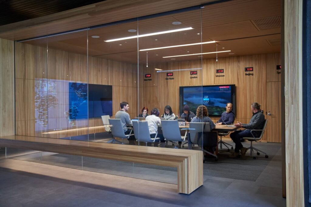 Conference room or board room meeting with people sitting around table in a room with international time clocks, and a map projection/reflection.