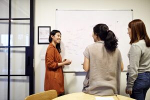 Three women grouped around whiteboard brainstorming ideas.