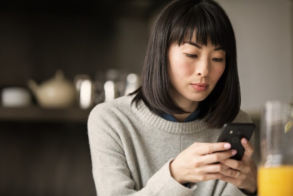 Adult female looking at phone with glass of juice in foreground.