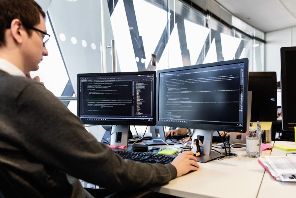 Male developer coding in front of two monitors at desk in office.