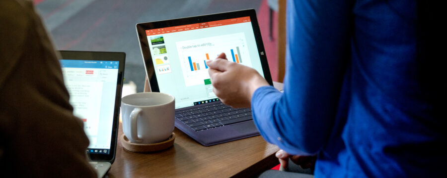 Two open laptops sitting on table in front of two figures, with a cup of coffee between them.