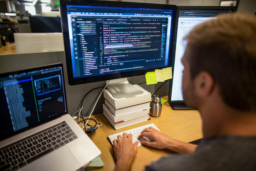 Photo of person typing into a keyboard and looking at a monitor on a desk