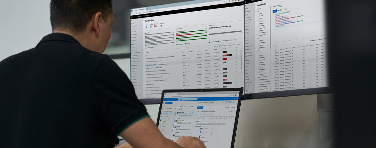 Security practitioner in front of two computer screens, working on their laptop to investigate threats.
