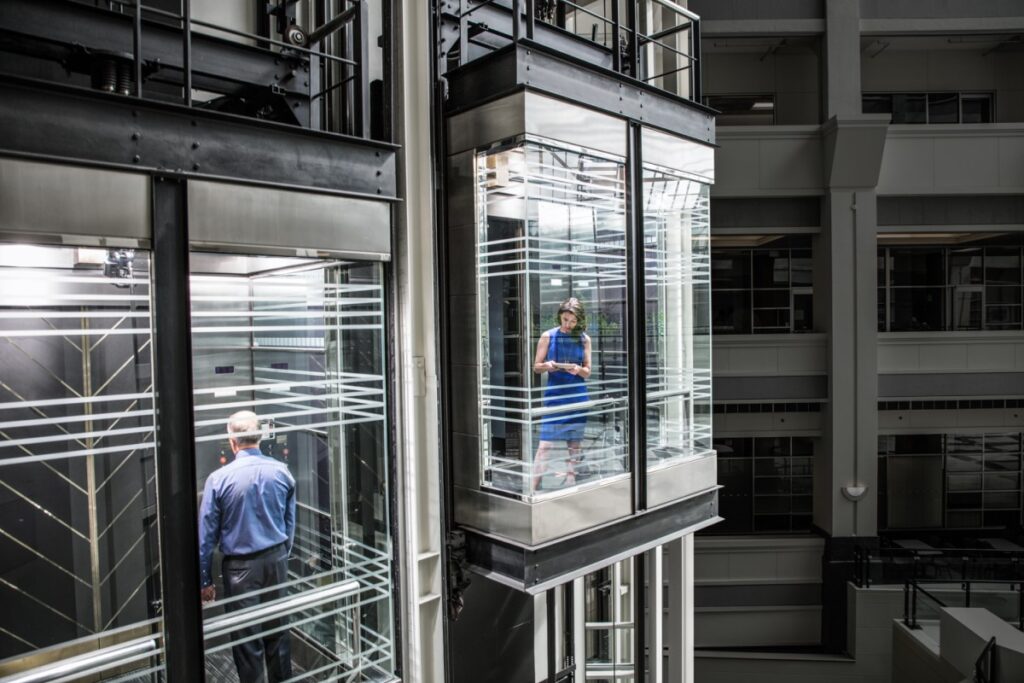 Business woman and man in separate glass elevators. The woman is using a Surface Pro.