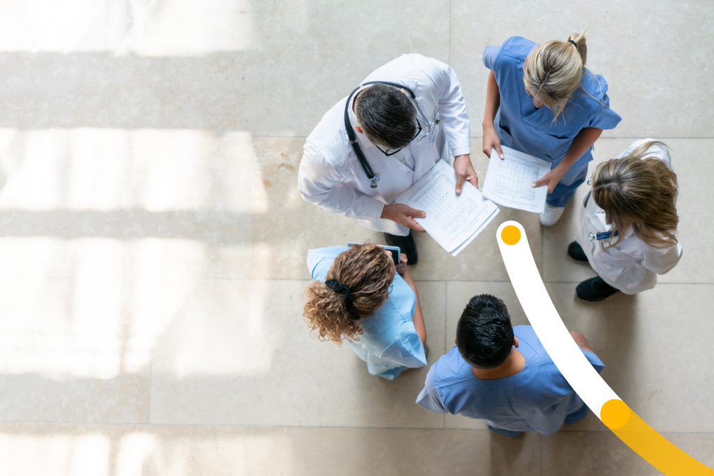 Five medical professionals standing in a circle reviewing a chart.