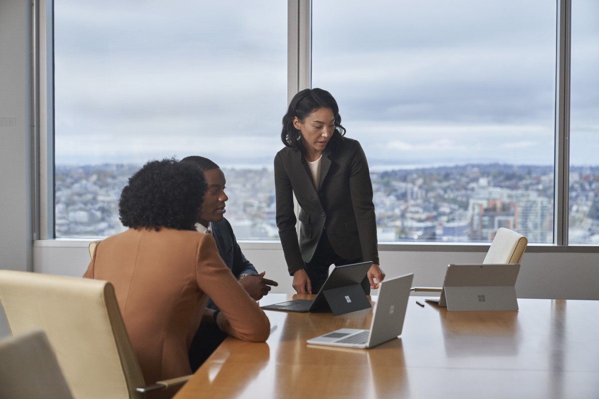 Conference room table with four people in a meeting with Surface Laptop Go 2 and Surface 2-in-1‘s.