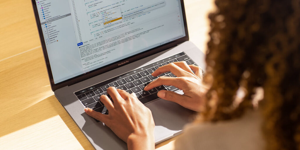 Black female developer coding on a MacBook Pro in the office, using Visual Studio.