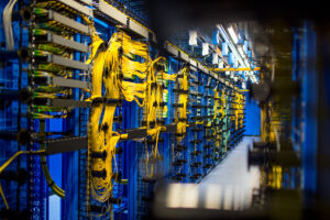 Data center illuminated with a bluish light. Yellow cords running on the servers are prominently displayed.
