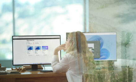A female architect sitting at an office desk showing Windows 365 and its Welcome screen on dual desktop monitors. Shown on Windows 11.