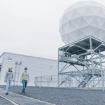 Photo of Orbital Ground Station satellite uplink. Two male datacenter employees walk side by side beneath the orbital ground station