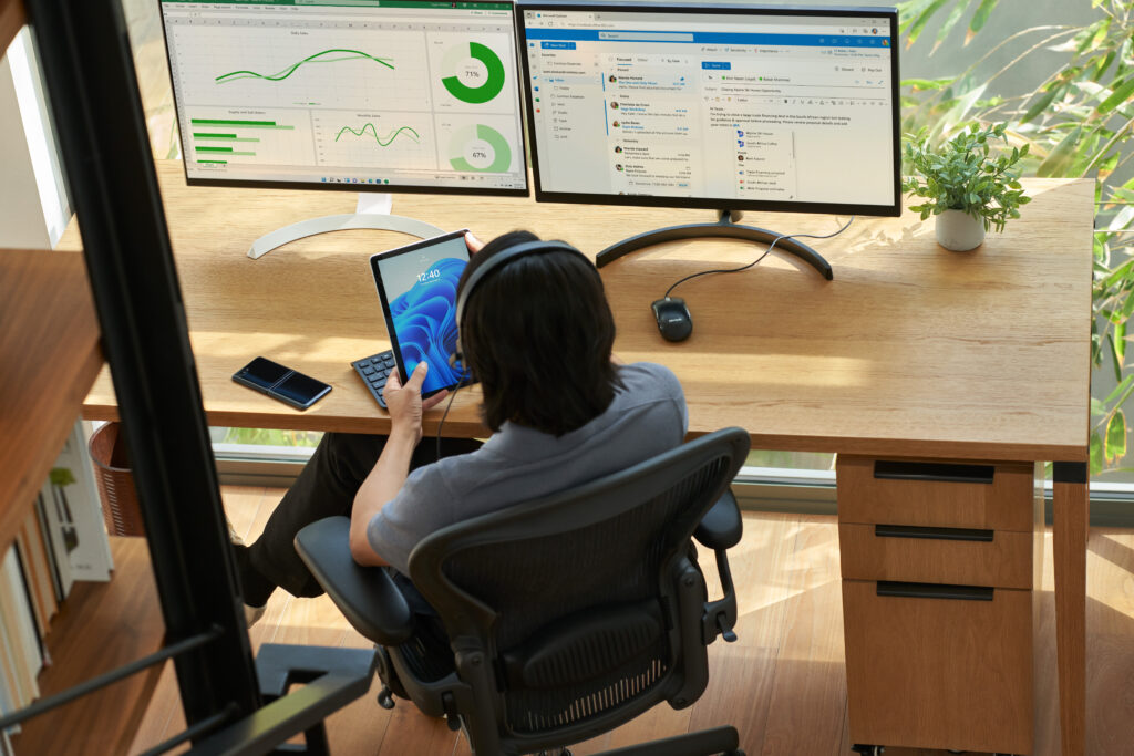 A man sitting at a computer holding a tablet.