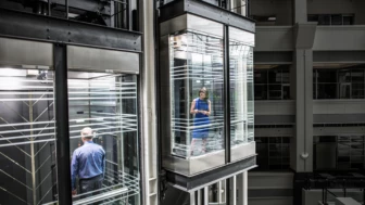 Photo of business woman and man in separate glass elevators.