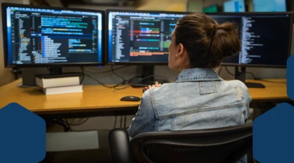 Photo of a developer coding her workspace in an enterprise office, using Visual Studio on a multi-monitor set up.