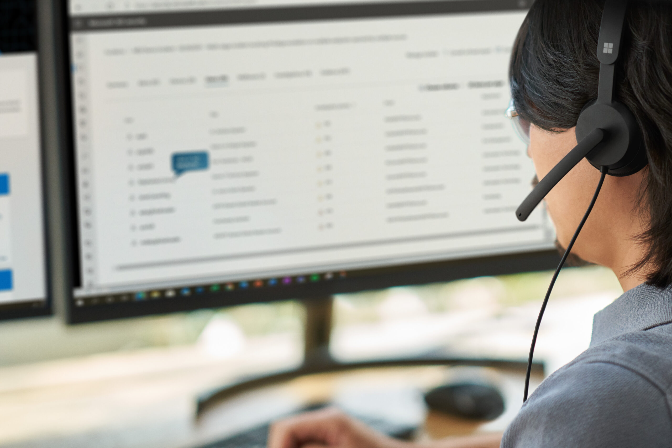 A woman wearing a headset and looking at a computer screen