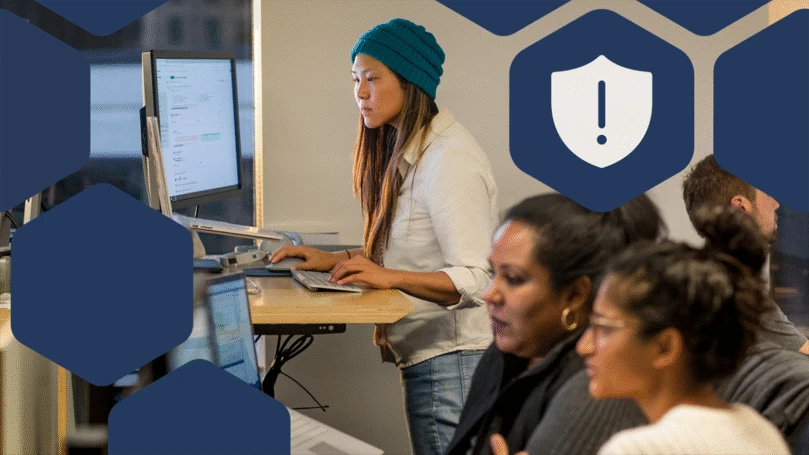 Female and male developers at work and collaborating. Some standing and some sitting using PC multi-monitor set ups.