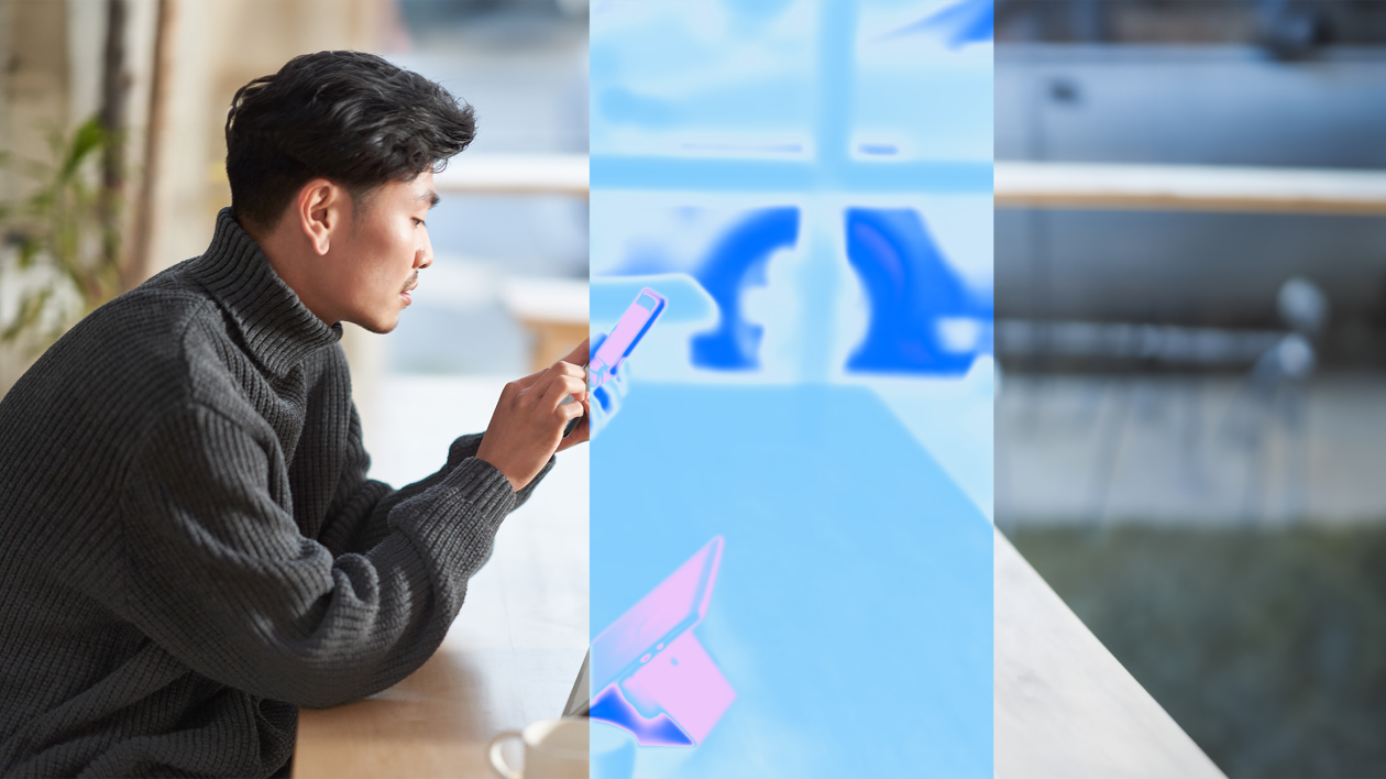 A man sitting at a laptop holding a cell phone.