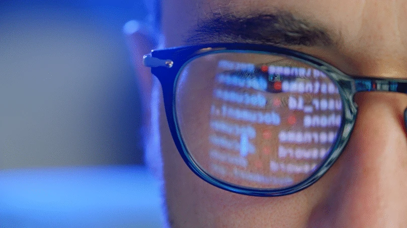 A person wearing glasses with code from a computer screen reflected in the lens.