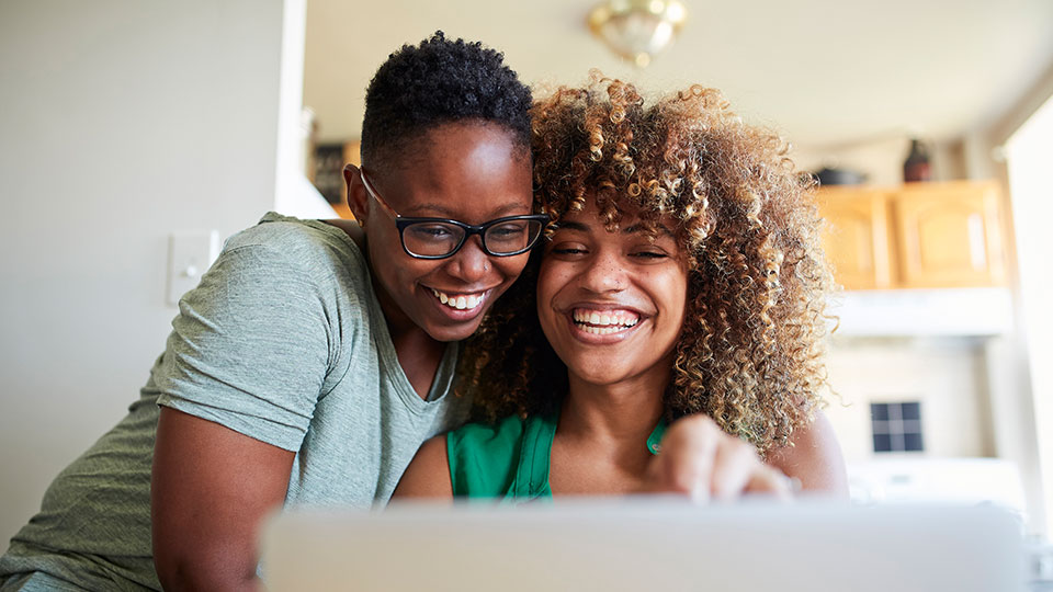 Two laughing women look at a laptop monitor