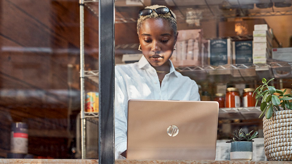 A woman seen through a window works on a laptop