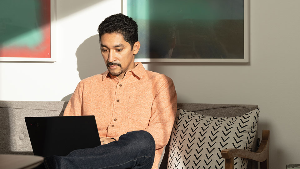 A man sitting on a sofa works on a laptop