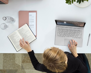 Overhead view of a person using a laptop while also looking up words in a dictionary