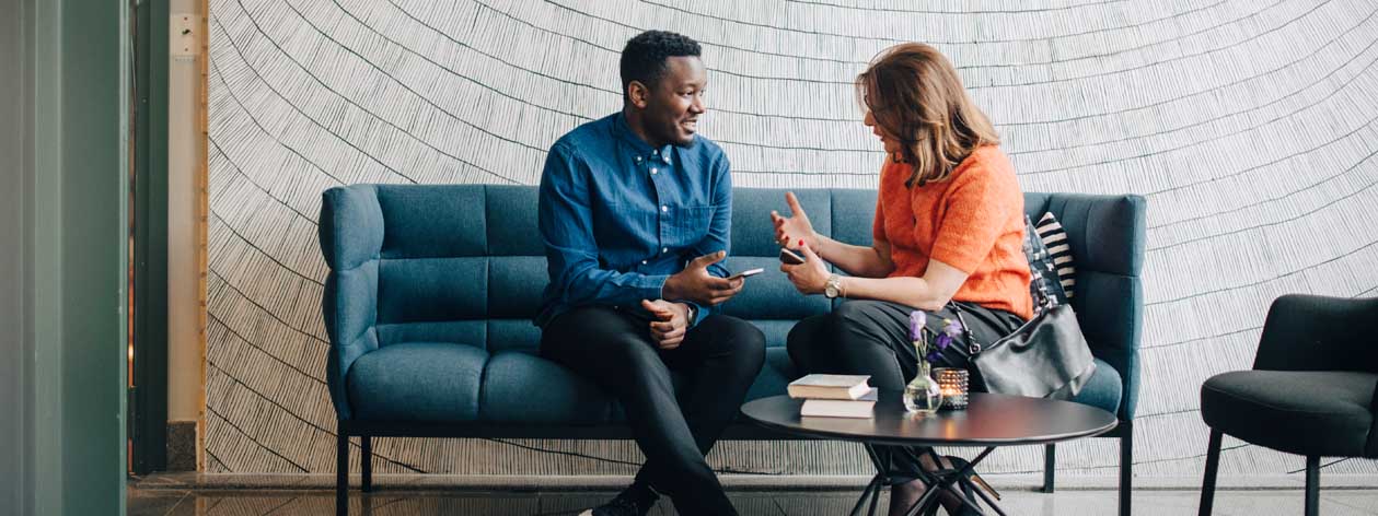 Two people sitting on a couch talking and using their mobile devices to communicate