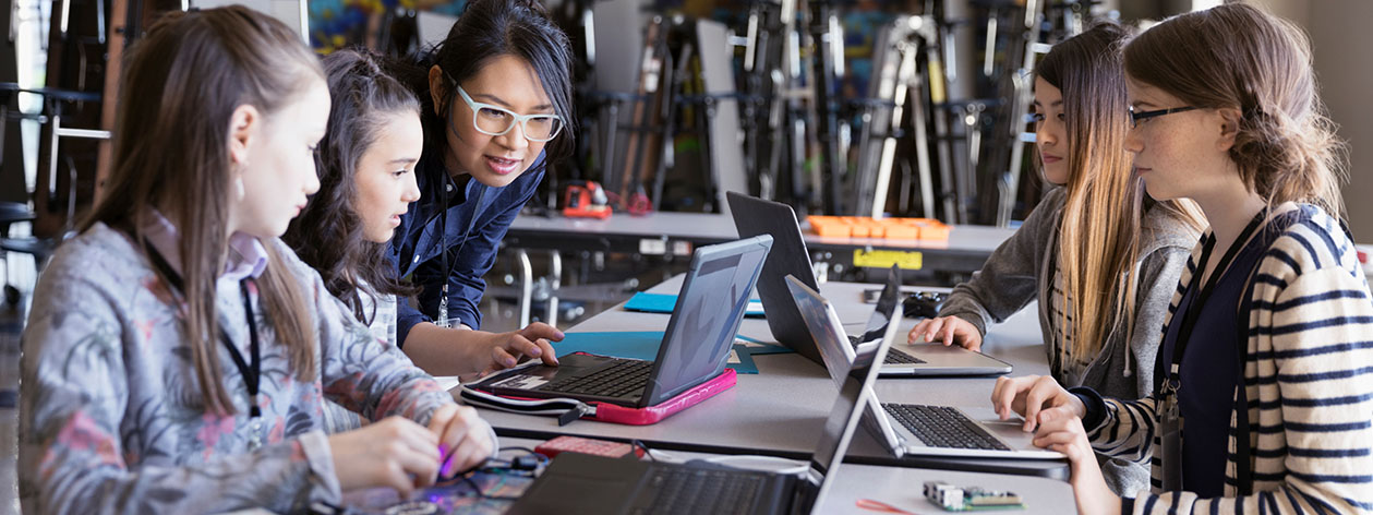 Professora com um grupo de meninas trabalhando em seus computadores