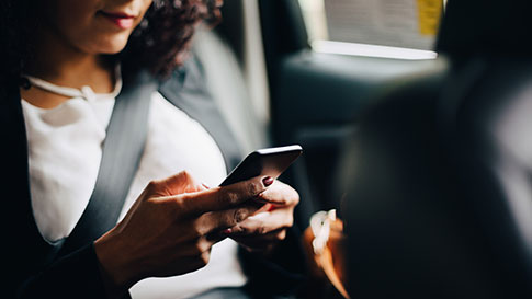 Eine Frau in einem Taxi schaut auf ihr Handy.