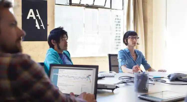 Several people sit around a conference table in a bright office, listening attentively.